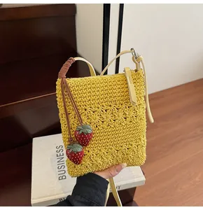 Detail of yellow hand-woven knit tote bag featuring red 3D strawberry pendants and long strap