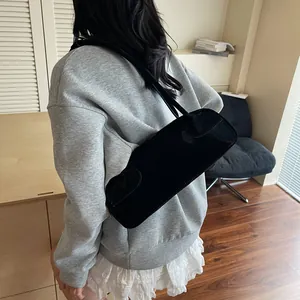 Sac baguette noir brillant au design minimaliste avec fines bandoulières porté par un modèle