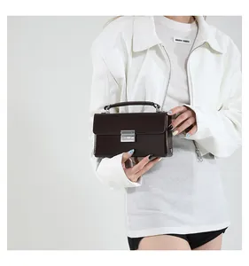Detail einer dunkelbraunen Box-Tasche aus Glattleder mit Silberschnalle an einem Model