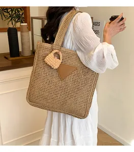 Détail d'un grand sac cabas en paille tissée avec empiècement cuir et charm en peluche au café