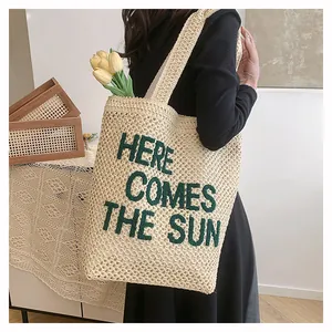 Detail of woven beach tote showing green 'HERE COMES THE SUN' embroidery and texture