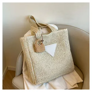 Détail du sac cabas en paille beige avec écusson triangulaire blanc en cuir et texture