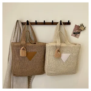 Détail du sac cabas en paille tressée avec empiècement triangle en cuir et bijou de sac