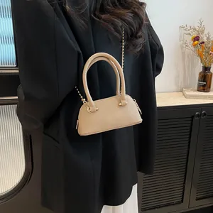 Chic beige lychee textured shell handbag with gold chain strap shown on black blazer