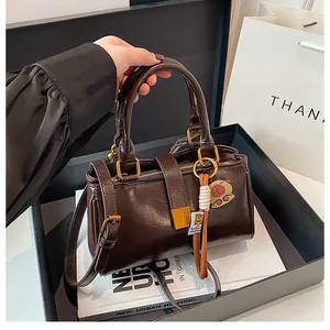 Detail of a dark brown glossy PU leather handbag with gold buckle and bear charm in a gift box