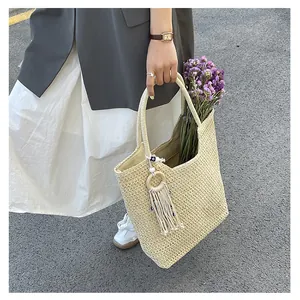 Detailed close-up of beige woven tote bag with fringe charm and wood ring accessory