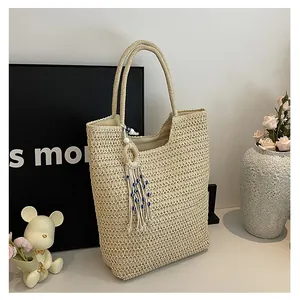 Detail of beige woven straw tote bag featuring decorative blue beaded fringe tassel