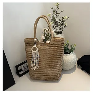 Close-up of beige woven tote bag with evil eye tassel detail on a minimalist white desk