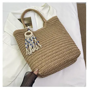 Close-up of straw woven tote bag featuring evil eye charm and white tassel detail