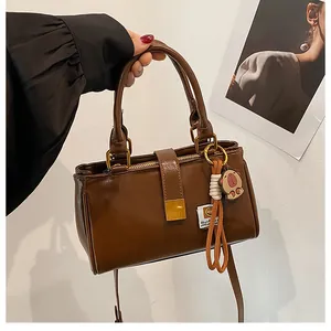 Detail view of brown leather handbag featuring gold buckle and cute piglet charm accessory