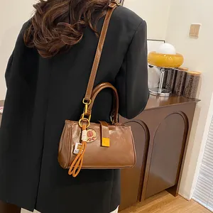 Brown leather shoulder bag with bear pendant and metal buckle shown on a model in a suit