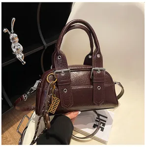 Détail d'un sac bandoulière marron foncé avec boucles argentées et breloque boulier
