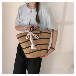 Détail du sac cabas en paille tissé à rayures noires avec un nœud en dentelle blanche