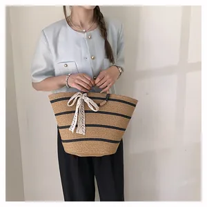 Détail d'un sac cabas en paille tressée avec rayures et un nœud en dentelle blanche