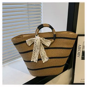 Détail du sac cabas en paille kaki avec rayures noires et nœud en dentelle blanche