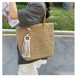 Detail einer großen Strohtasche mit braunen Ledergriffen und Fransenanhänger für Damen