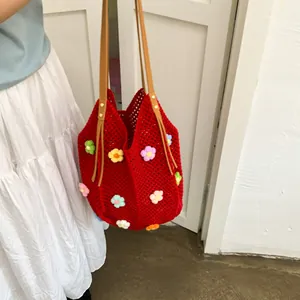Detail of red crochet tote bag with 3D floral accents and brown leather shoulder strap