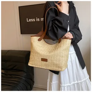 Détail du sac cabas en paille tissée avec anses en cuir marron et étiquette de mode devant