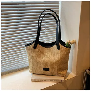 Détail du sac cabas en paille tissée avec anses en cuir noir et étiquette FASHION