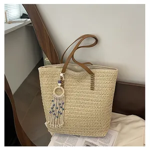 Detail der beigen Stroh-Stofftasche mit braunen Kunstledergriffen und Evil-Eye-Anhänger