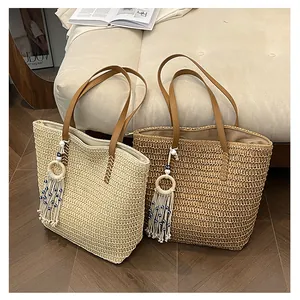 Detail der gewebten Stroh-Tote-Bag mit braunem Lederriemen und Boho-Quastenanhänger