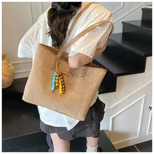 Detail of a large straw tote bag with leather handles and bohemian beaded tassel charm