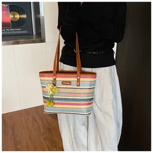 Detail of colorful rainbow striped straw tote bag with brown leather handles and flower charm