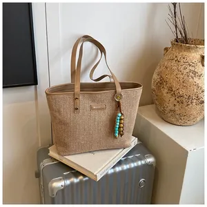 Detail of straw woven tote bag with beaded charm on art book and travel suitcase