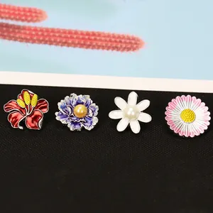 Detailset aus vier Emaille-Blumenbroschen mit Perlenmitte auf einer schwarzen Unterlage