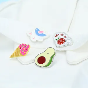 Dettaglio di spille in smalto con avocado, gelato, uccellino e coccinella su tessuto