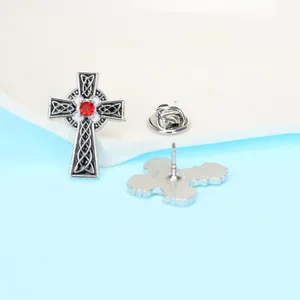 Détail d'une broche croix celtique argentée vintage avec strass rouge et attache papillon