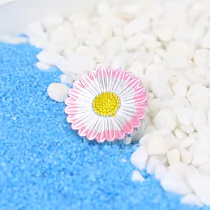 Exquisite Brosche in Pink und Weiß mit Emaille-Gänseblümchen auf blauem Sandhintergrund