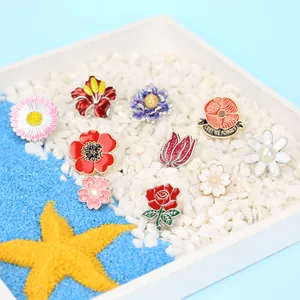 Nahaufnahme von Emaille-Blumen-Pins mit Rosen- und Gänseblümchen-Designs auf Steinen
