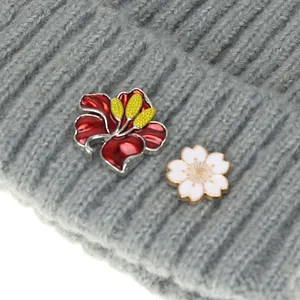 Nahaufnahme von roten und weißen Emaille-Blumen-Pins an einer grauen Strickmütze