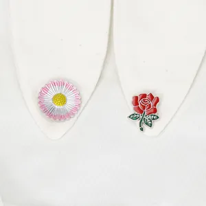 Detail von Emaille-Blumen-Anstecknadeln mit rosa Gänseblümchen und roter Rose auf Stoff