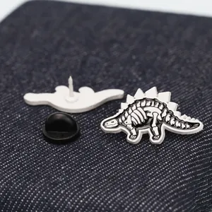 Macro view of black and white dinosaur skeleton enamel pin with secure rubber back