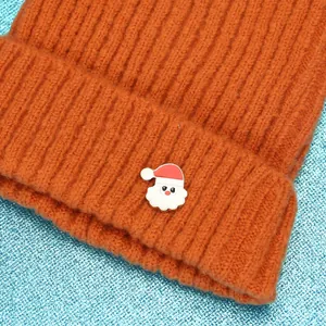 Détail du pin's Père Noël en émail sur un bonnet en maille orange à grosses côtes