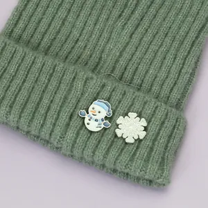 Détail d'un bonnet en maille verte avec broche émaillée bonhomme de neige et flocon