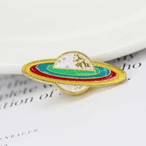 Vue macro d'un pin's Saturne en émail avec anneaux colorés et détails en métal doré