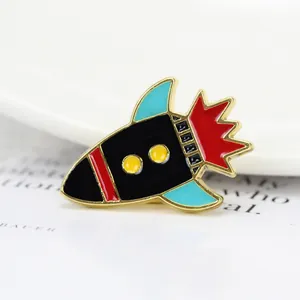 Gros plan d'un pin's fusée en émail avec bordure dorée et détails colorés