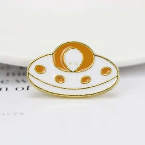 Vue macro d'un pin's OVNI émaillé orange et blanc avec une finition en métal doré