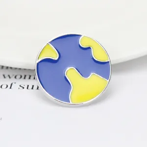 Gros plan d'un pin's rond en émail avec un design de carte du monde bleu et jaune