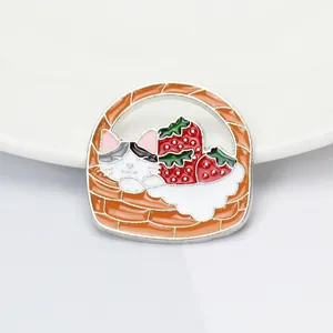 Détail d'un pin's émaillé montrant un chat et des fraises dans un panier