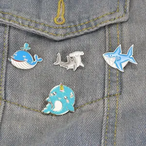 Cartoon ocean creature enamel pins with sharks and whales on a blue denim jacket