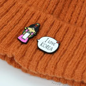 Makroansicht einer Cartoon-Mädchennadel und I LOVE KOREA Abzeichen auf einer Strickmütze
