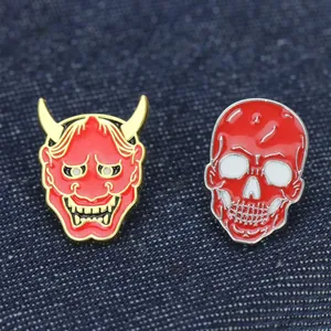 Dettaglio di spillette smaltate rosse a forma di teschio e maschera Hannya su denim
