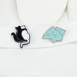 Close-up of enamel pins featuring black and white cats and blue geometric heart smile symbols