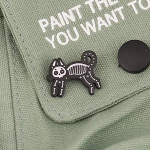 Punk skeleton cat enamel pin in black and white pinned to a canvas bag fabric