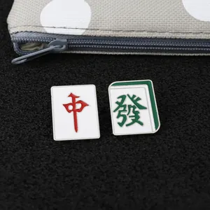 Gros plan de pins Mahjong en émail avec caractères rouges et verts sur fond noir texturé