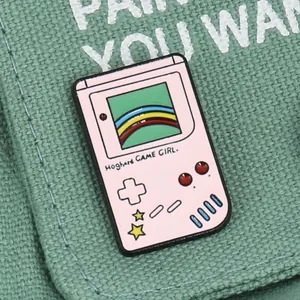 Macro shot of pink retro handheld game console enamel pin on canvas fabric texture